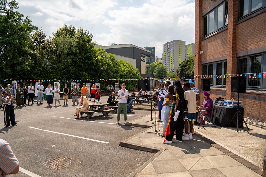 Colourful flag bunting and an audience watching a group of people singing outside North Street building during celebrations of International Day 2024