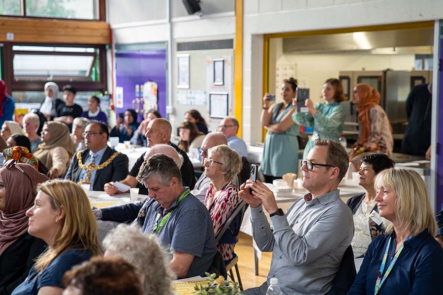A room full of audience members including Keighley Mayor and Keighley College Principal Kevin O Hare sat on chairs looking at a stage during Keighley College Refugee Week 2024